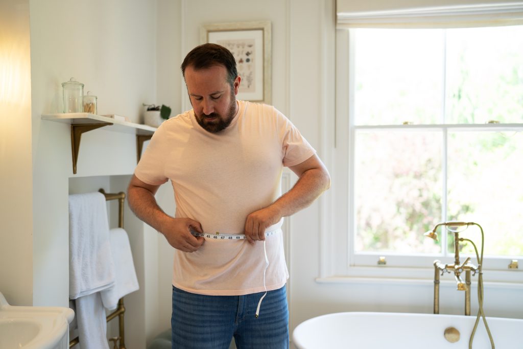 Man measuring waist in bathroom