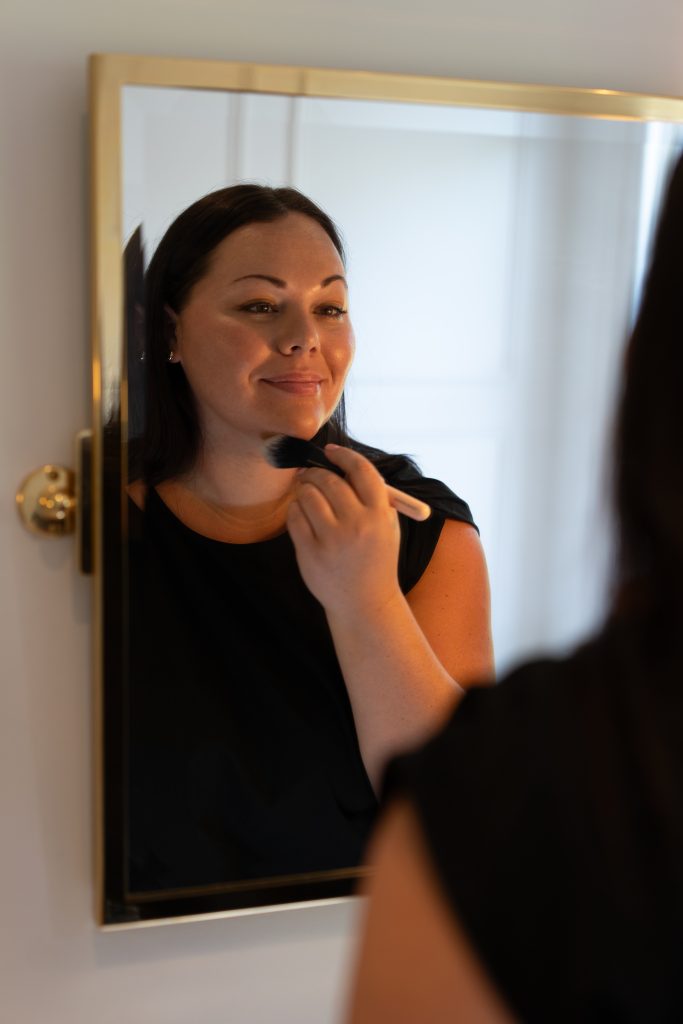 Smiling women, applying makeup in the mirror.